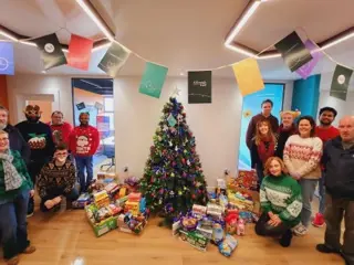 13 Ardonagh Analytics on give back day, around a Christmas tree with their food donation to Ken Smollen who help Irish families  