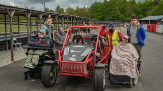 A group of Speed of Sight beneficiaries, including disabled and visually impaired people, with a car.