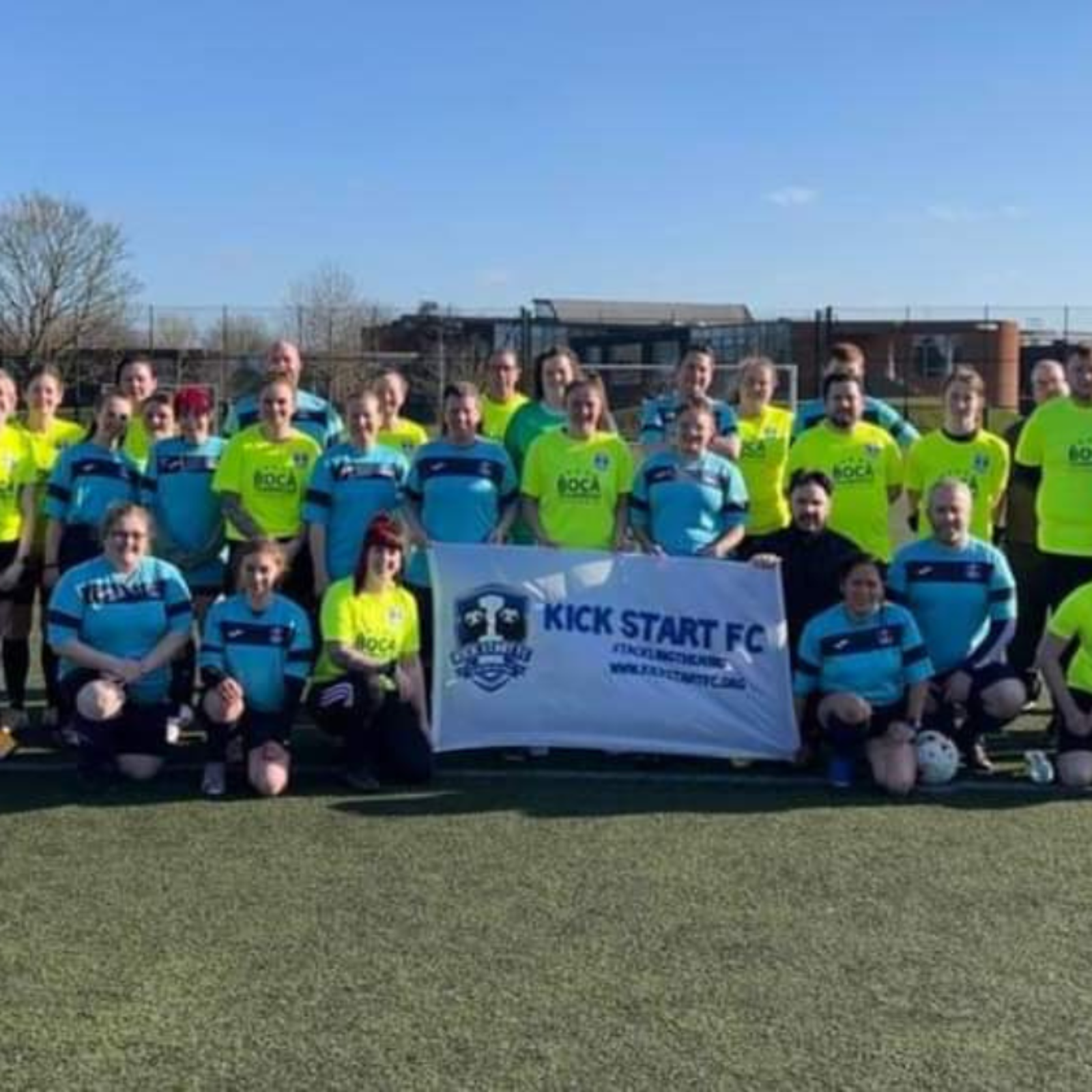 Kick Start FC team stood on football pitch holding up a banner