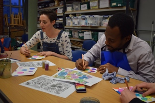 A woman and a man painting pictures whilst sat at a table.